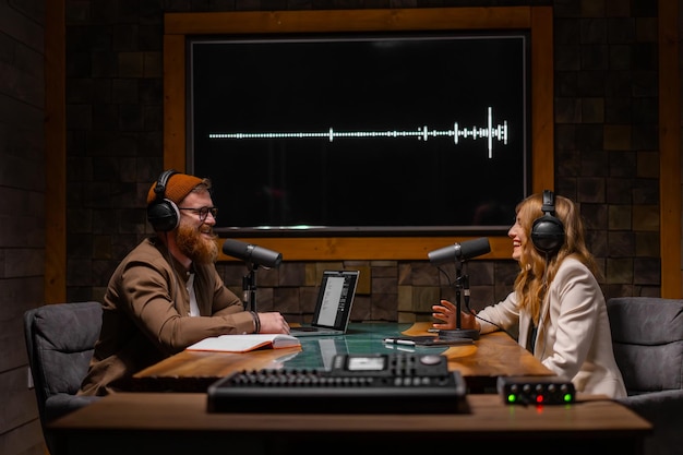 Deux animateurs de radio parlent et sourient alors qu'ils sont assis près des microphones dans un studio de radiodiffusion créatif