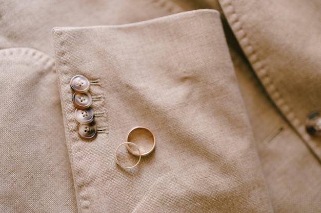 Deux anneaux de mariage en or sur la manche d'une veste homme beige avec des boutons