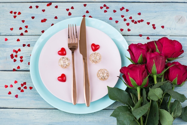 deux assiettes, des couverts, un bouquet de roses et de coeurs