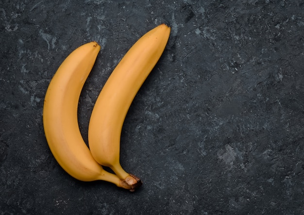 Deux bananes sur une table en béton noir. Fruits tropicaux. Tendance du minimalisme. Vue de dessus.