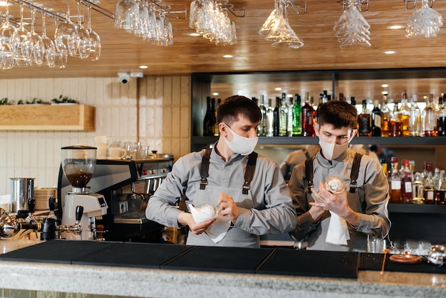 Deux barmans élégants en masques et uniformes pendant la pandémie frottent des verres pour briller Le travail des restaurants et des cafés pendant la pandémie