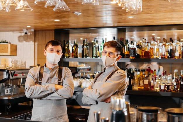 Deux barmans élégants, masqués et uniformes pendant la pandémie, se tiennent derrière le bar. Le travail des restaurants et cafés pendant la pandémie.