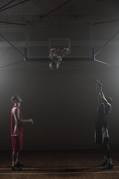 Deux basketteurs dans un gymnase dont un marque un shoot