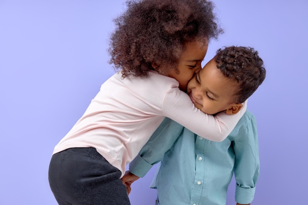 Deux beaux frères et sœurs noirs américains, soeur embrassant son frère, isolés sur violet