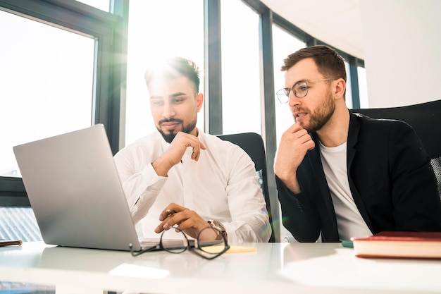 Deux beaux hommes d'affaires travaillent ensemble sur un ordinateur portable