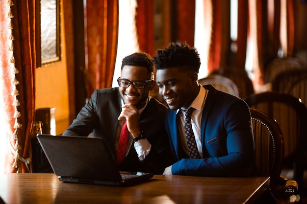 Deux beaux hommes africains à l'intérieur avec un ordinateur portable