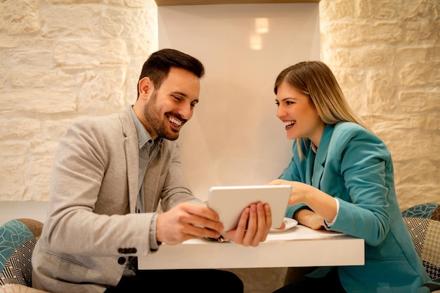 Photo deux beaux jeunes hommes d'affaires souriants assis au café et travaillant sur une tablette numérique.