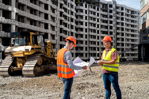 Deux beaux ouvriers en uniforme sur un chantier de construction réfléchissent à un plan. Équipement de construction