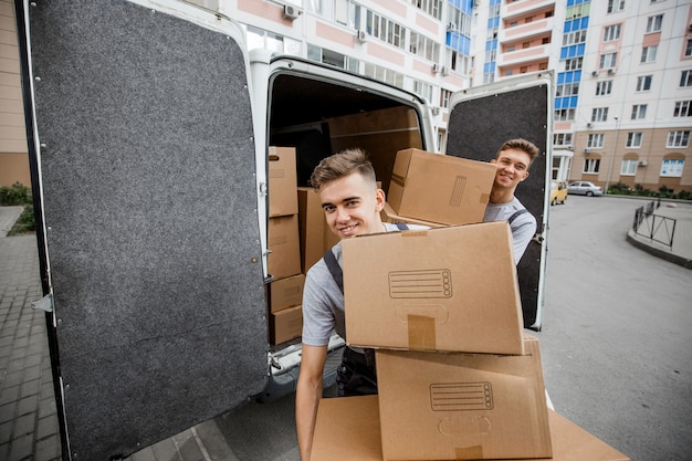 Deux beaux ouvriers en uniforme déchargent la camionnette pleine de cartons