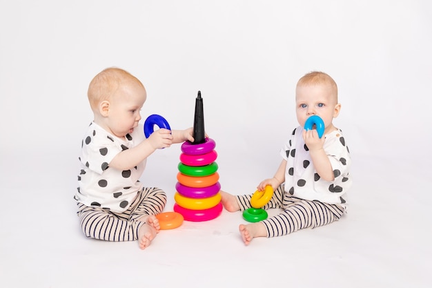 Deux bébés jumeaux de 8 mois jouent sur un fond blanc isolé, développement précoce des enfants jusqu'à un an, un enfant prend un jouet d'un autre, une place pour le texte