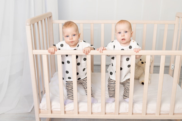 Deux bébés jumeaux frère et sœur de 8 mois sont assis en pyjama dans le berceau et regardent la caméra, vue de dessus, le concept d'amitié, une place pour le texte.