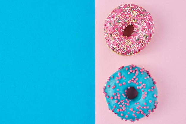 Deux beignets glacés avec des paillettes sur fond rose et bleu avec espace copie, vue de dessus à plat. Concept de minimalisme