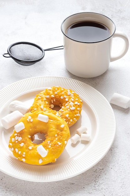 Photo deux beignets jaunes glacés avec des guimauves et une tasse de thé ou de café petit-déjeuner ou collation servi