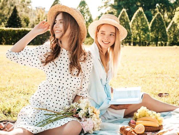 Deux belle jeune femme hipster en robe d'été à la mode et chapeaux. Femmes insouciantes faisant un pique-nique à l'extérieur.