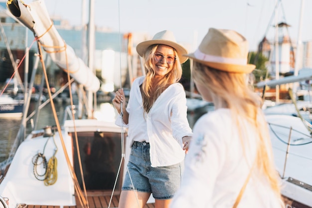 Deux belles amies blondes mère et fille en chapeaux blancs et paille sur le yacht à la jetée