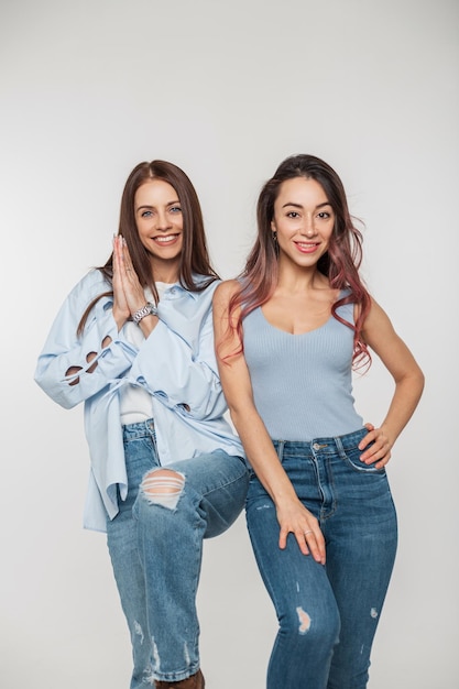 Deux belles amies heureuses dans des vêtements en denim décontractés de mode avec des jeans posant sur un fond blanc