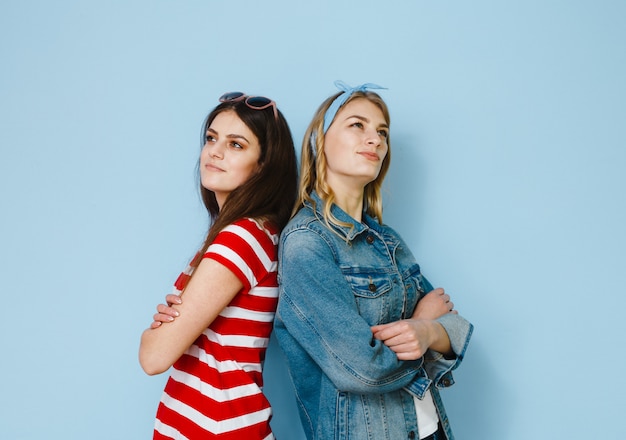 Deux belles copines s'amusent et montrent des gestes sur un fond bleu