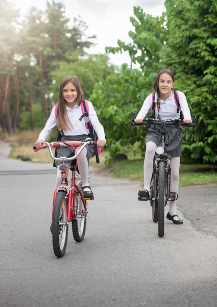 Deux belles écolières souriantes allant à l'école à vélo