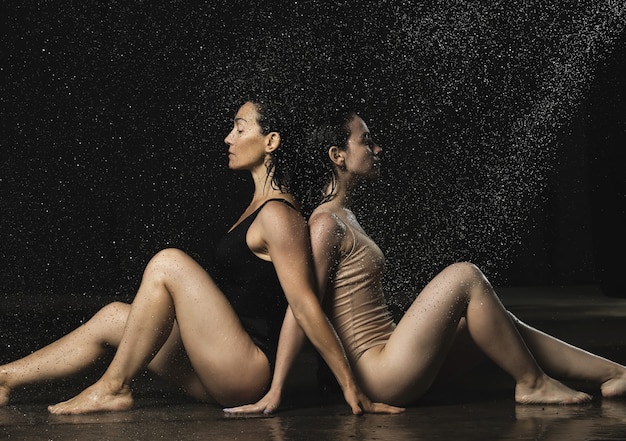 Deux belles femmes d'apparence caucasienne aux cheveux noirs s'assoient dos à dos dans des gouttes d'eau