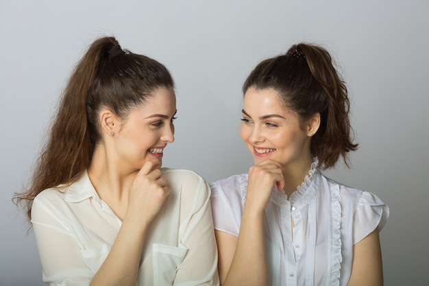 Deux belles femmes joyeuses jumelles sur fond gris