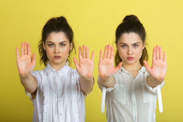 Deux belles femmes joyeuses jumelles sur fond jaune avec le geste de la main