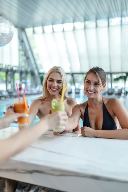 Deux belles femmes se relaxant à la piscine avec des cocktails. Belles jeunes femmes buvant des cocktails au bar de la piscine