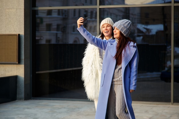 Deux Belles Filles En Bonnets De Laine Prenant Selfie à L'aide D'un Smartphone à L'extérieur En Hiver