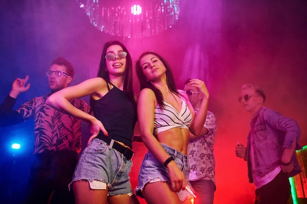 Deux belles filles dansant devant des jeunes qui s'amusent dans une boîte de nuit avec des lumières laser colorées