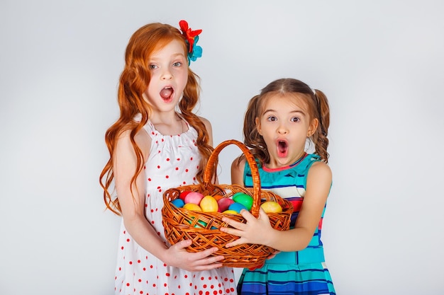 Photo deux belles filles lumineuses tenant un panier d'oeufs de pâques. moments marrants. fond blanc. concept de vacances de printemps. célébration de pâques en famille.