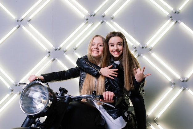 Deux belles filles portant des costumes de coureurs et assis sur une moto, dans le studio