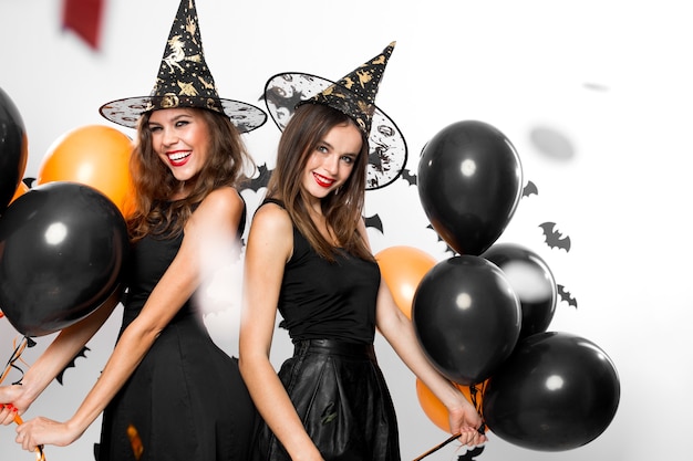 Deux belles filles en robes noires et chapeaux de sorcière s'amusent avec des ballons noirs et oranges. Halloween .