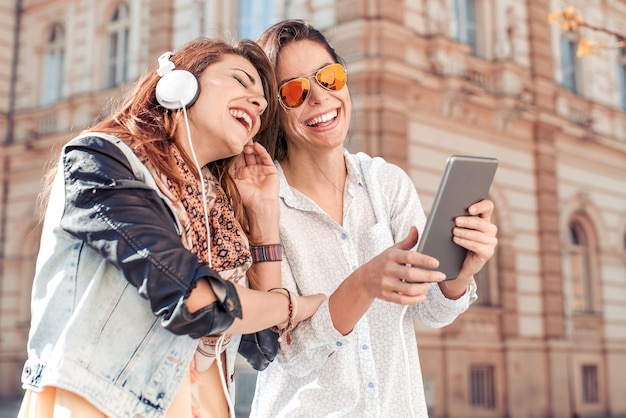 Deux belles filles en ville écoutant de la musique sur une tablette numérique