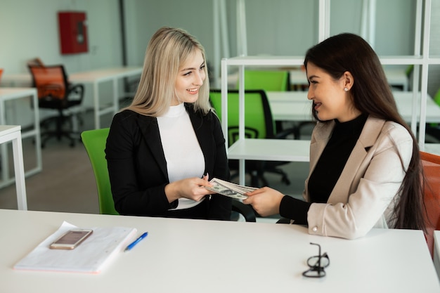 deux belles jeunes femmes au bureau à la table avec des dollars