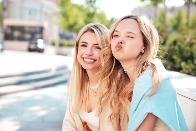 Deux belles jeunes femmes hipsters souriantes en vêtements d'été à la mode posant sur le fond de la rue