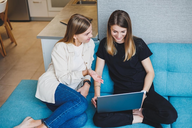 Deux belles jeunes femmes utilisant un ordinateur portable regardant un film assis sur un canapé à la maison deux amies assises sur un canapé à la maison dans le salon