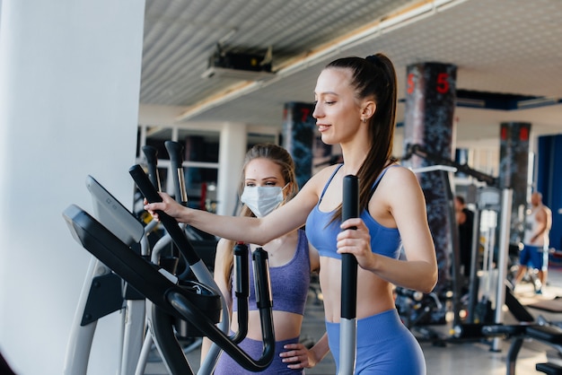 Deux belles jeunes filles font de l'exercice dans la salle de sport avec des masques pendant la pandémie