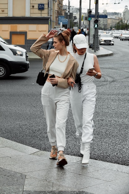 Deux belles jeunes filles à la mode posant dans la rue. Des mannequins portant des lunettes de soleil élégantes et des vêtements de couleur claire. Mode de vie en ville. Concept de mode féminine et d'amis.