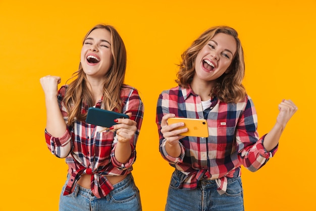 deux belles jeunes filles portant des chemises à carreaux s'amusant et jouant à des jeux vidéo sur des téléphones portables isolés