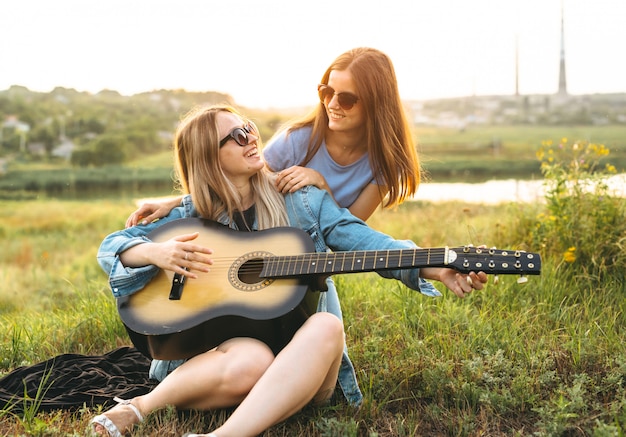 Deux belles jeunes filles profitant de leur temps ensemble et jouant de la guitare au coucher du soleil