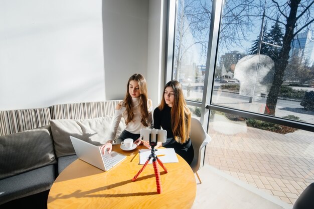 Deux belles jeunes filles sont assises dans un café, enregistrent des blogs vidéo et communiquent sur les réseaux sociaux.