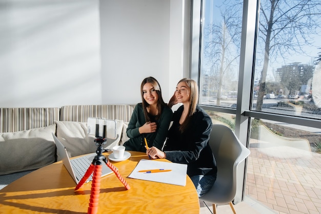 Deux belles jeunes filles sont assises dans un café, enregistrent des blogs vidéo et communiquent sur les réseaux sociaux.