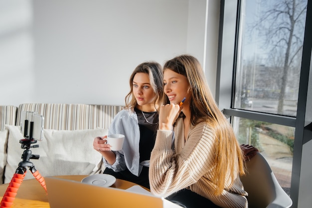 Deux belles jeunes filles sont assises dans un café, enregistrent des blogs vidéo et communiquent sur les réseaux sociaux.