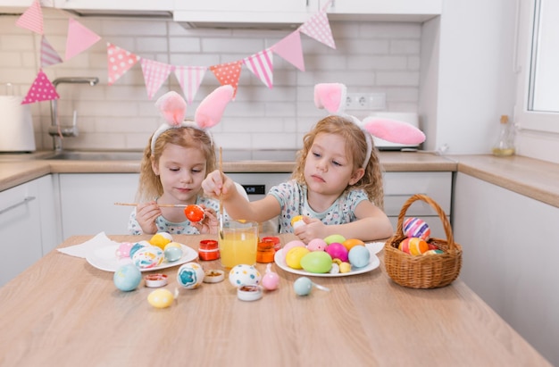 Deux belles petites filles jumelles dessinent des oeufs de Pâques Une famille heureuse se prépare pour Pâques deux mignonnes petites filles avec des oreilles de lapin le jour de Pâques