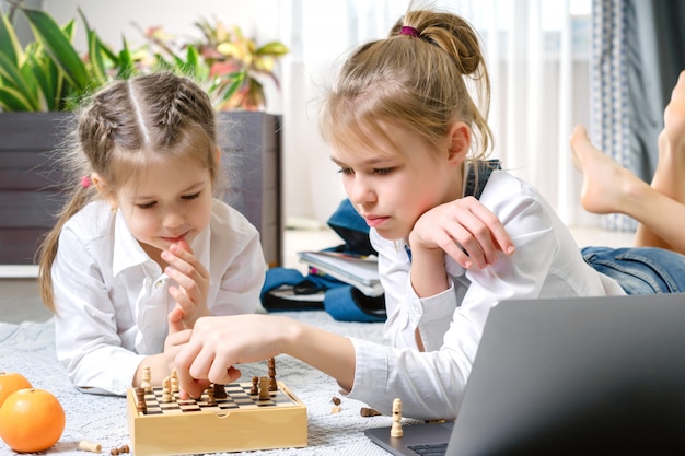 Deux belles petites soeurs jouant aux échecs sur un étage dans le salon