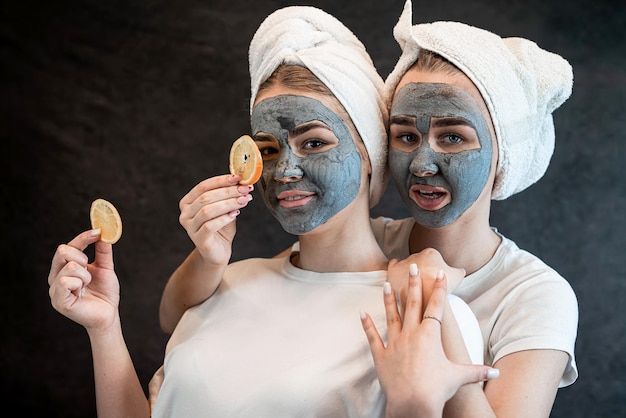 Deux belles soeurs appliquant un masque d'argile noire et tenant des morceaux d'orange isolés sur noir