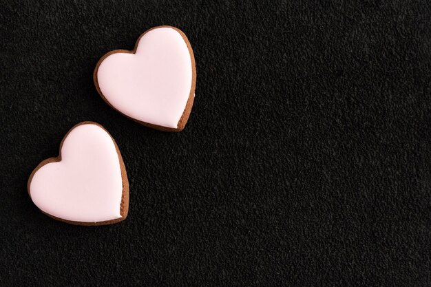 Deux biscuits en forme de coeur glacés blancs sur fond noir Copiez l'espace