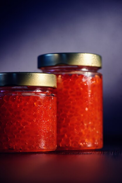 Photo deux bocaux en verre fermés pleins de caviar rouge avec couvercle en métal sur fond sombre