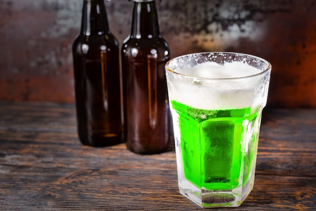 Deux bouteilles de bière à côté de verre avec une bière verte et une tête de mousse sur le vieux bureau sombre. Concept de boissons et de boissons