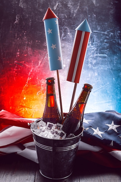 Deux bouteilles de bière dans un seau à glace avec le drapeau américain à proximité et des fusées pour les feux d'artifice. Concept de célébration de la fête de l'indépendance