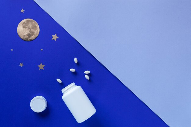 Deux bouteilles blanches, pilules, lune sur fond bleu. Concept Insomnie, pleine lune, troubles du sommeil, somnolence. Maquette, vue de dessus, mise à plat, espace de copie.